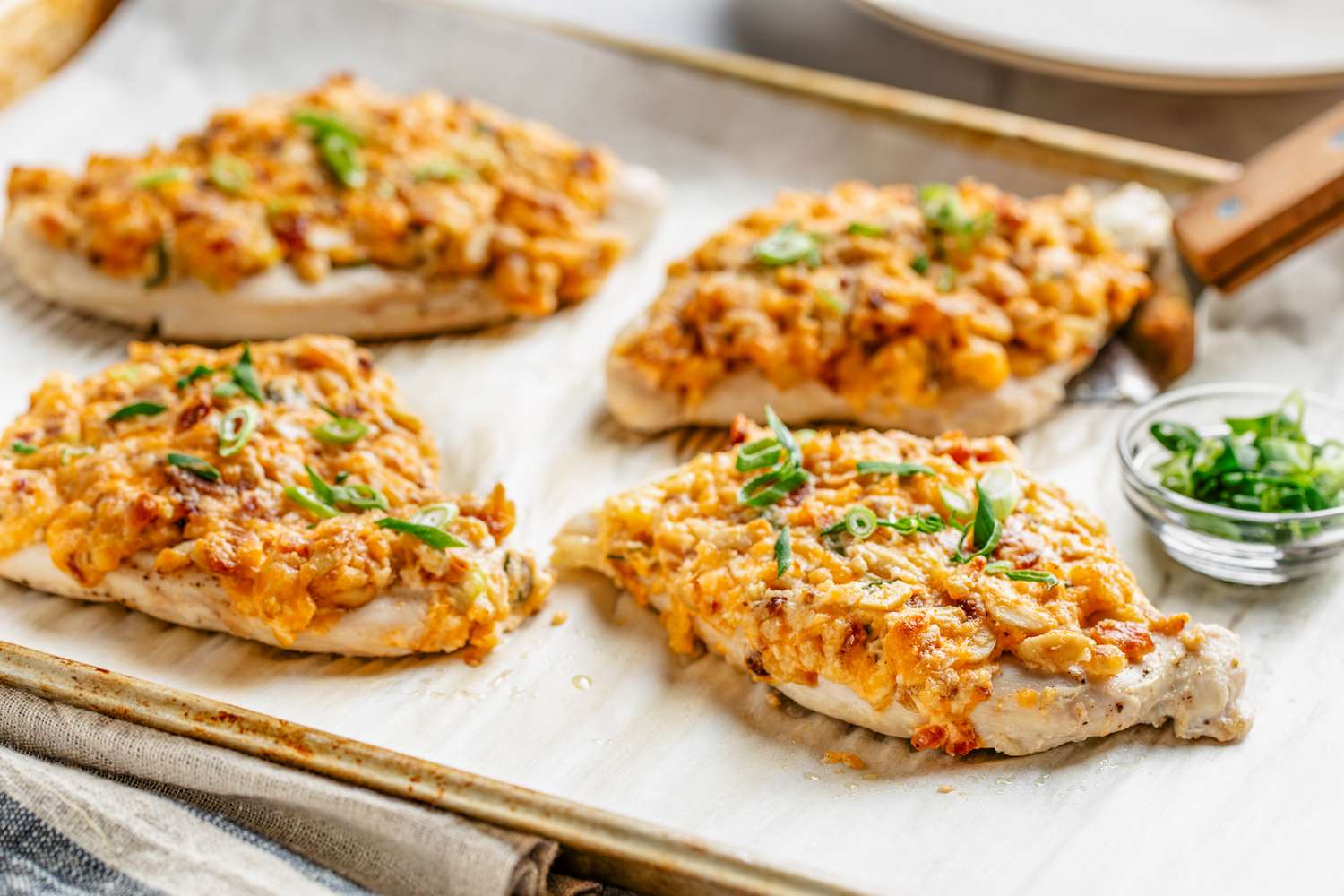Million dollar chicken on a parchment lined baking sheet with a bowl of sliced scallions
