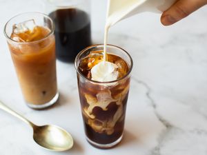 A hand pouring a pitcher of creamer into a glass of iced coffee
