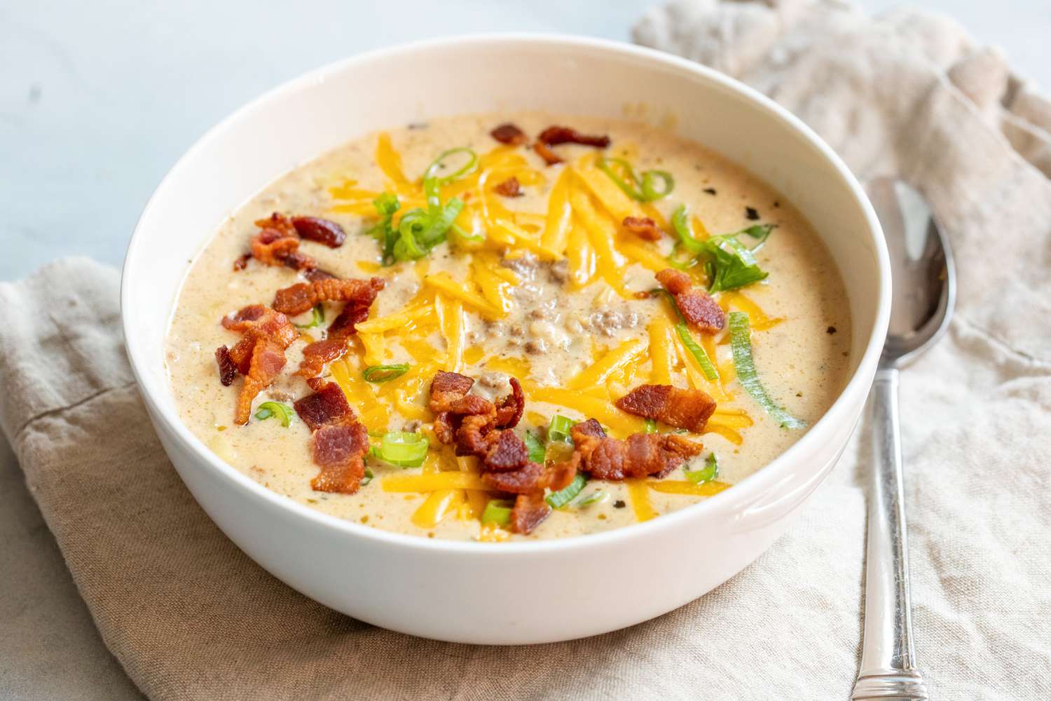Cheesy bacon cheeseburger soup in soup bowl and with spoon.