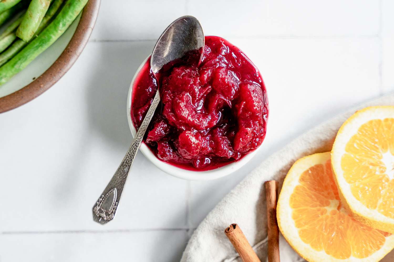 Instant Pot Cranberry Sauce Next to a Bowl of Green Beans and Table Napkin with Orange Slices and Cinnamon Sticks