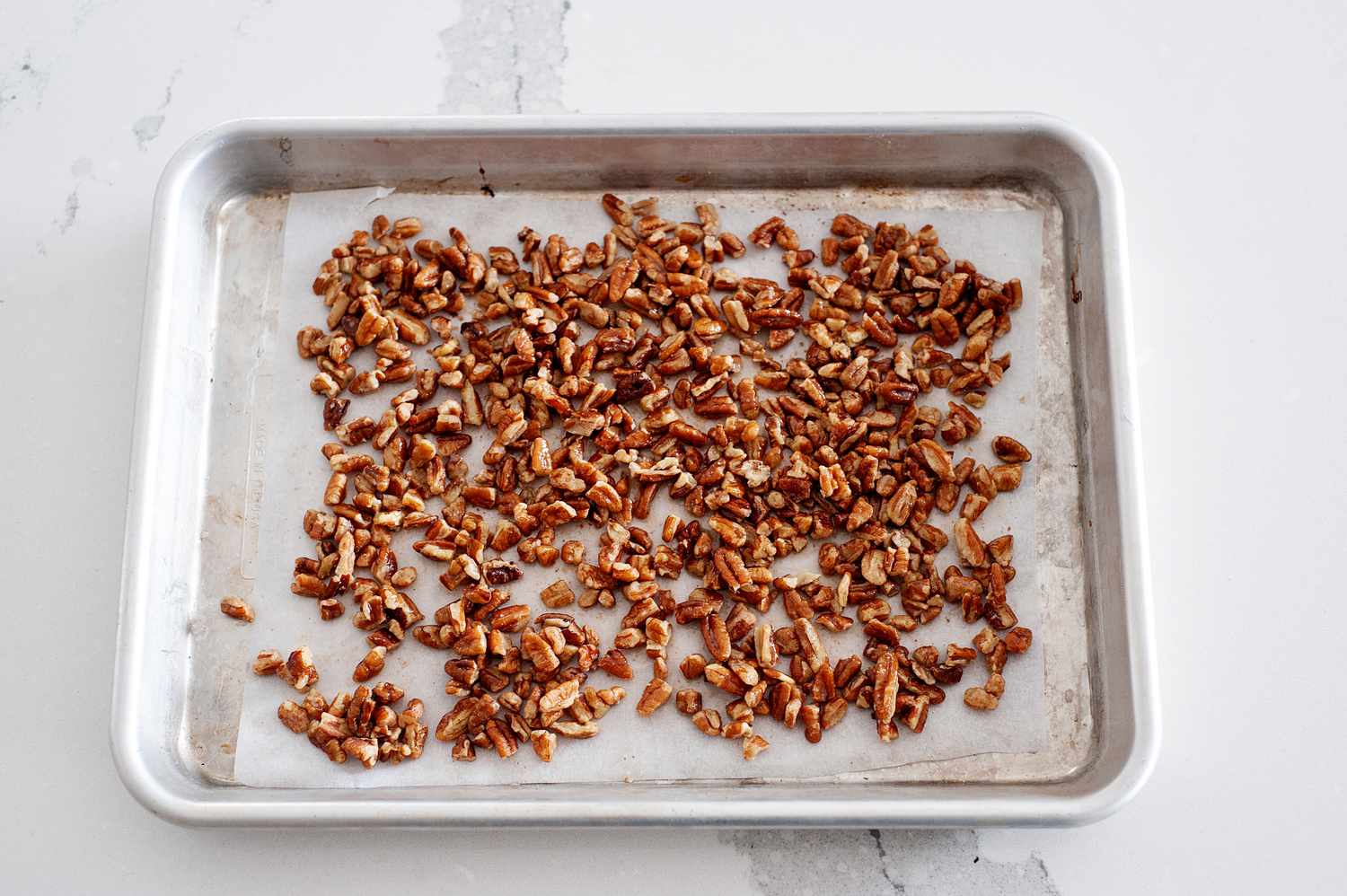 Toasting pecans on a baking sheet to make a butter pecan ice cream recipe.