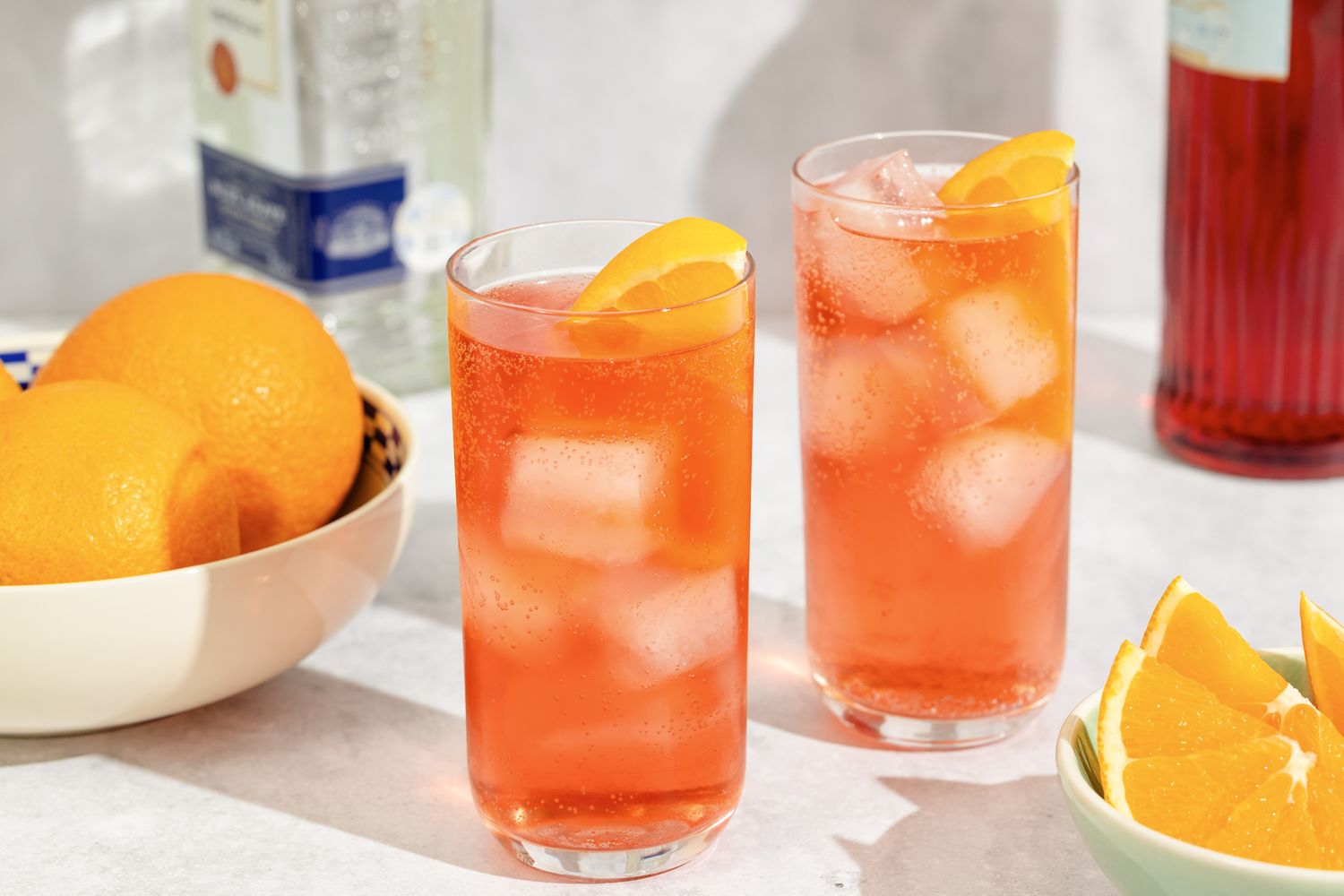Two cocktails with ice and orange slices garnish bowls nearby