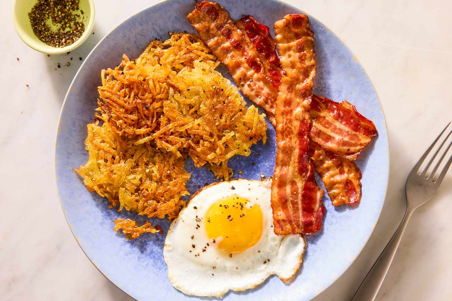 Plate of hash browns fried egg and crispy bacon with a fork