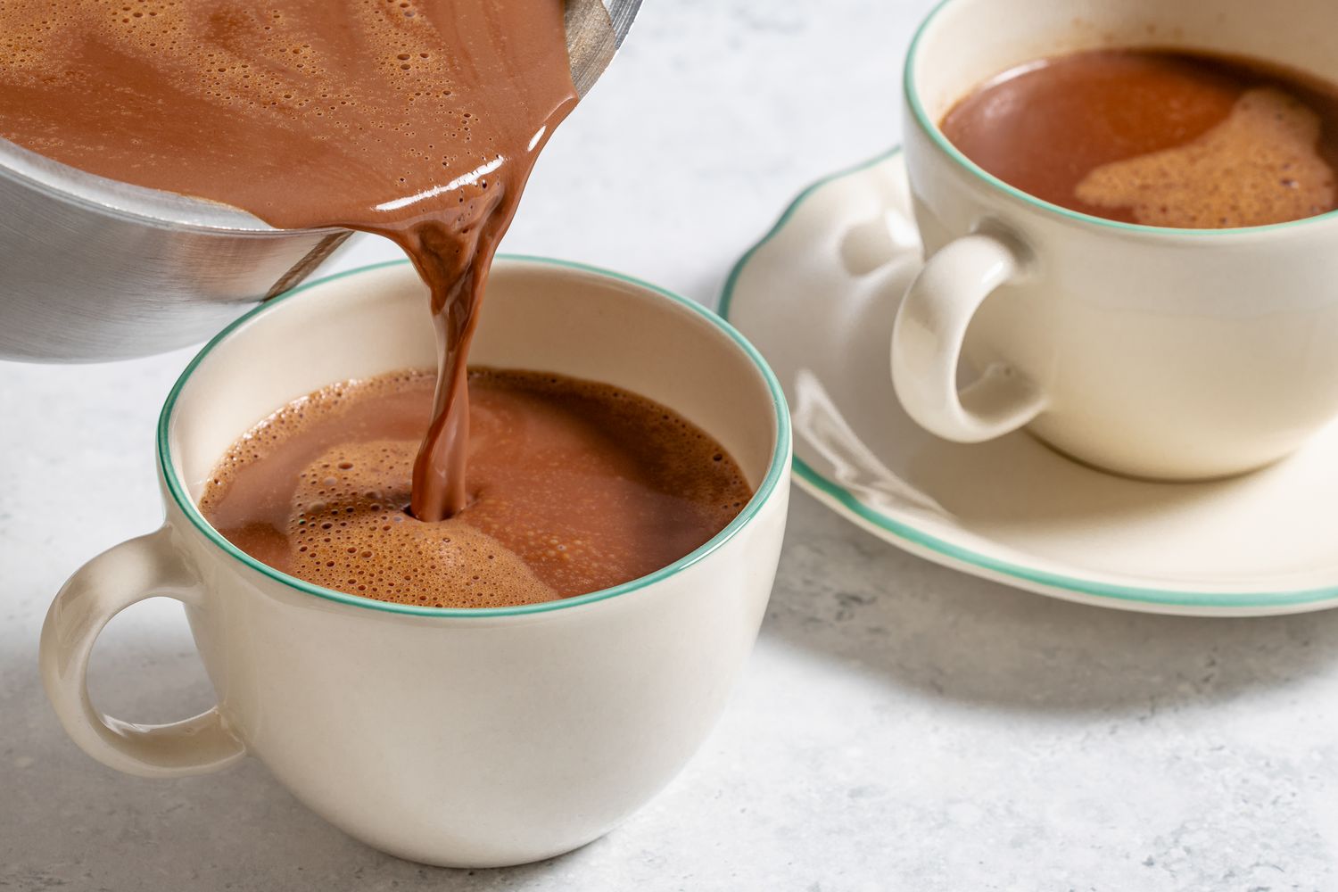 Pouring hot chocolate into a cup with another filled cup in the background