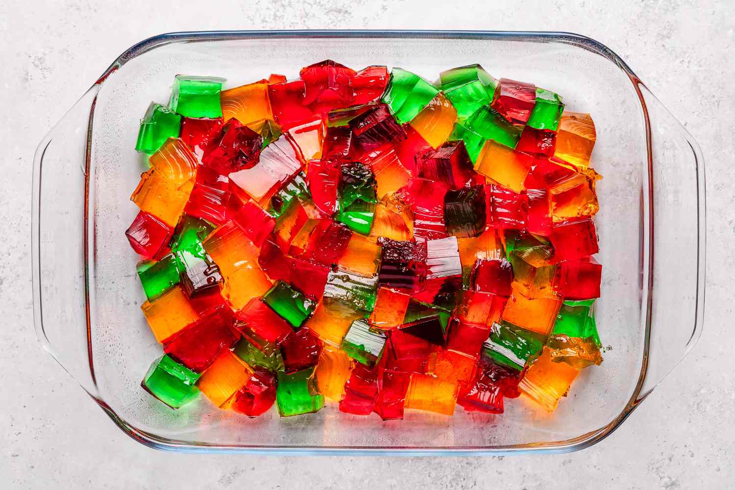 Overhead shot of different colored jello squares in a rectangular clear baking dish for the stained glass jello recipe