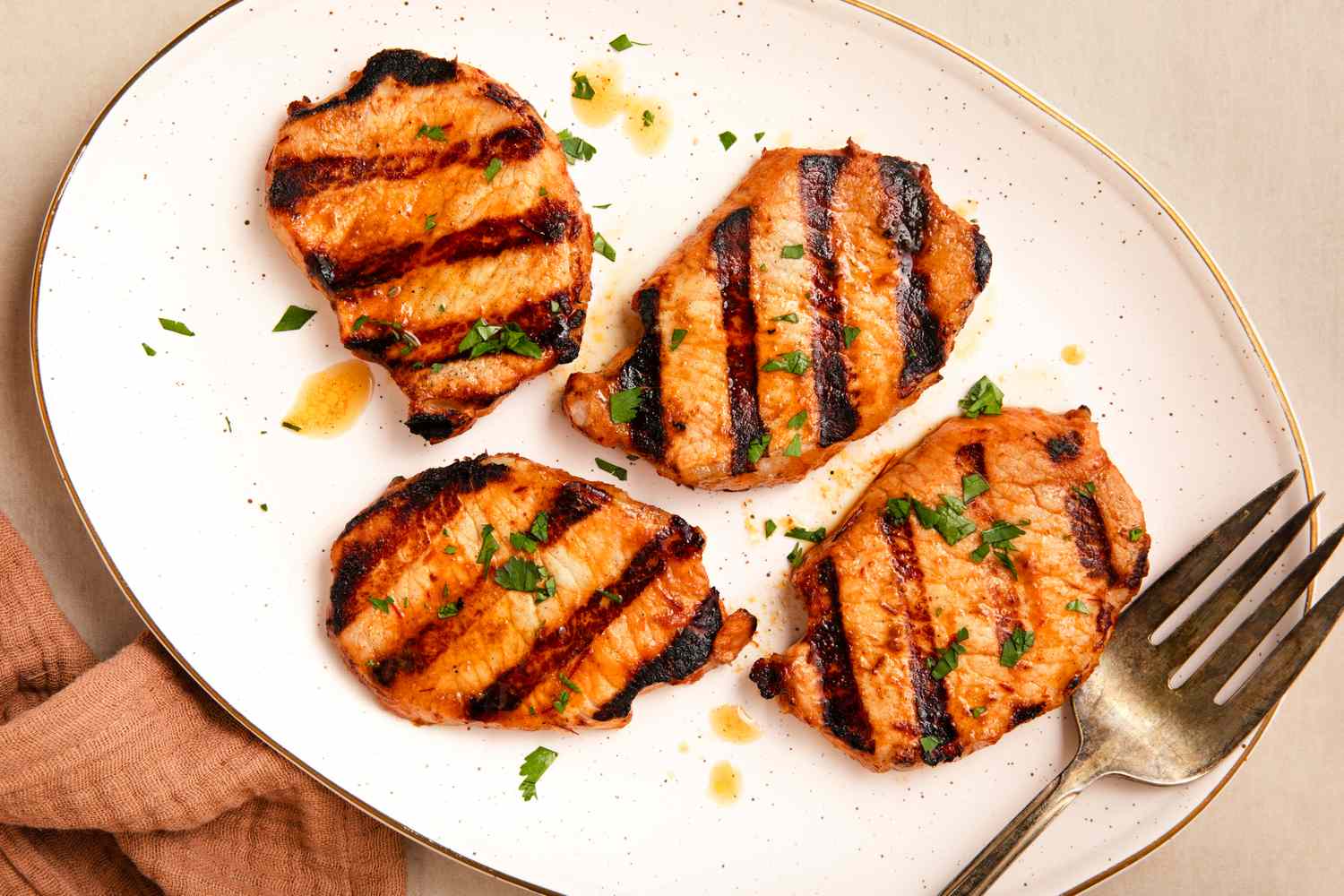 Grilled pork chops garnished with herbs on a white plate fork and napkin alongside