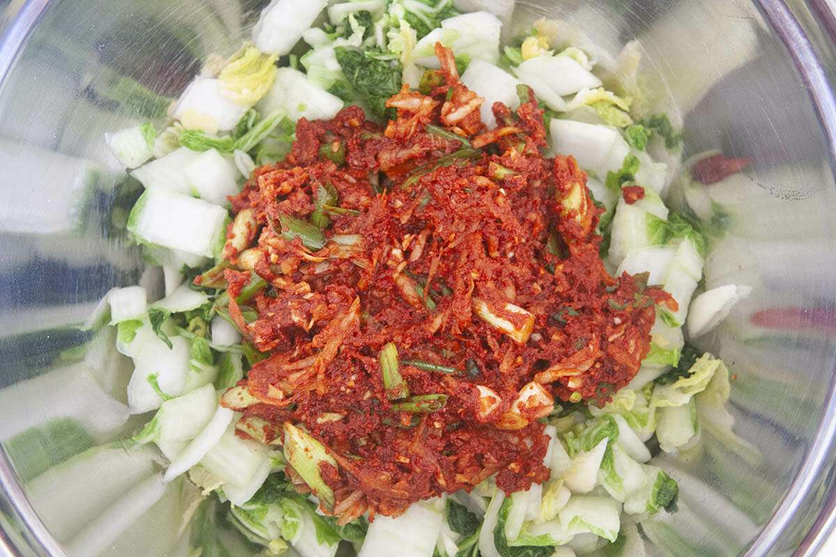 A metal mixing bowl with ingredients to show how to make kimchi.