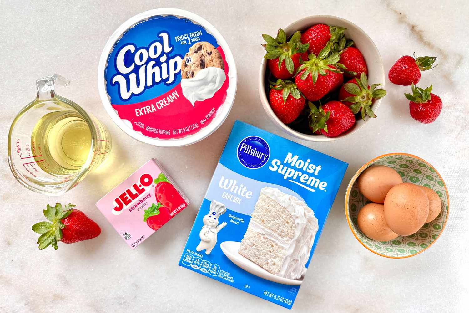 Ingredients for a strawberry cake including cake mix, Jello, Cool Whip, and strawberries