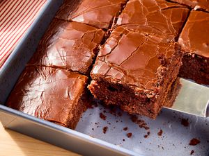 Metal baking pan of sliced coca cola cake with a slice being removed with a metal spatula