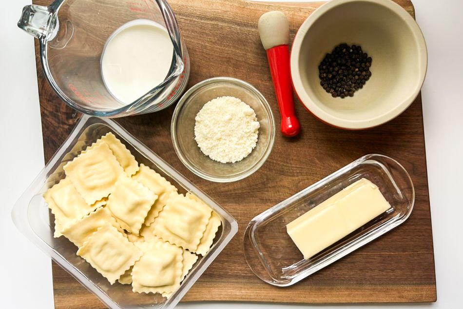 Ingredients including ravioli butter cream pepper and cheese on a wooden board