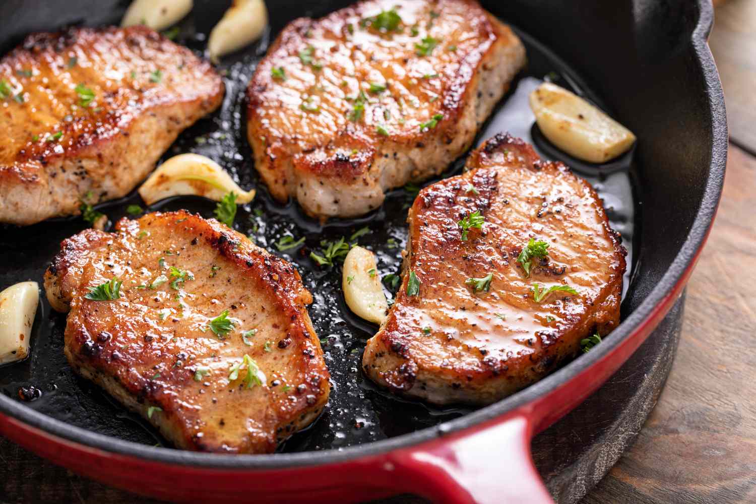 Seared pork chops in a skillet with roasted garlic and garnish