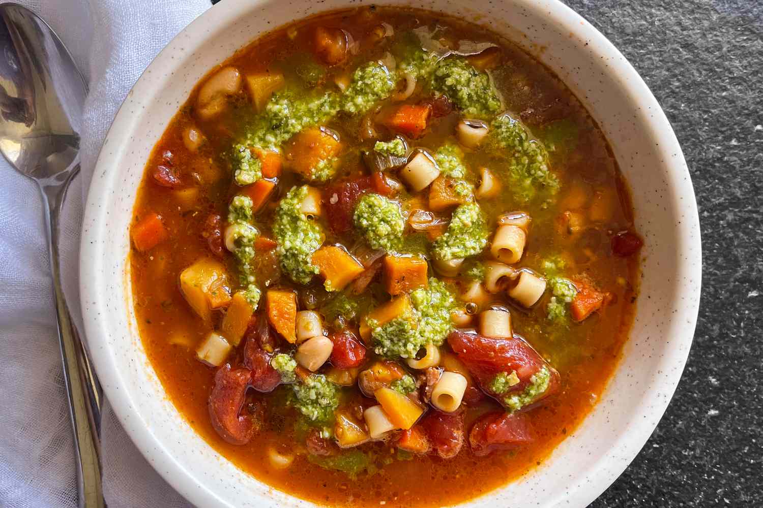 A bowl of minestrone, showing a swirl of green pesto on top