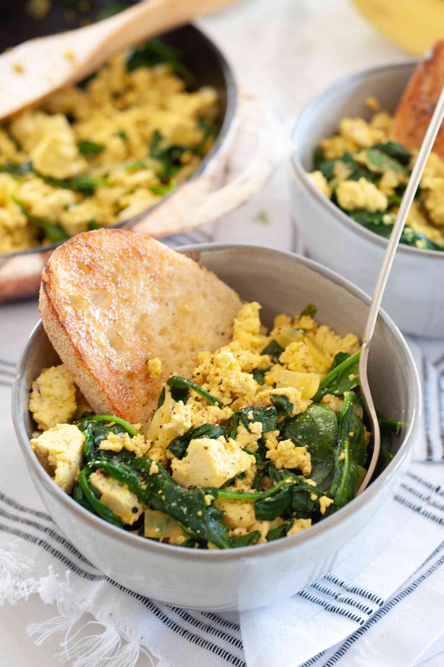 Vegan spinach and tofu scramble in small bowl with toast. 