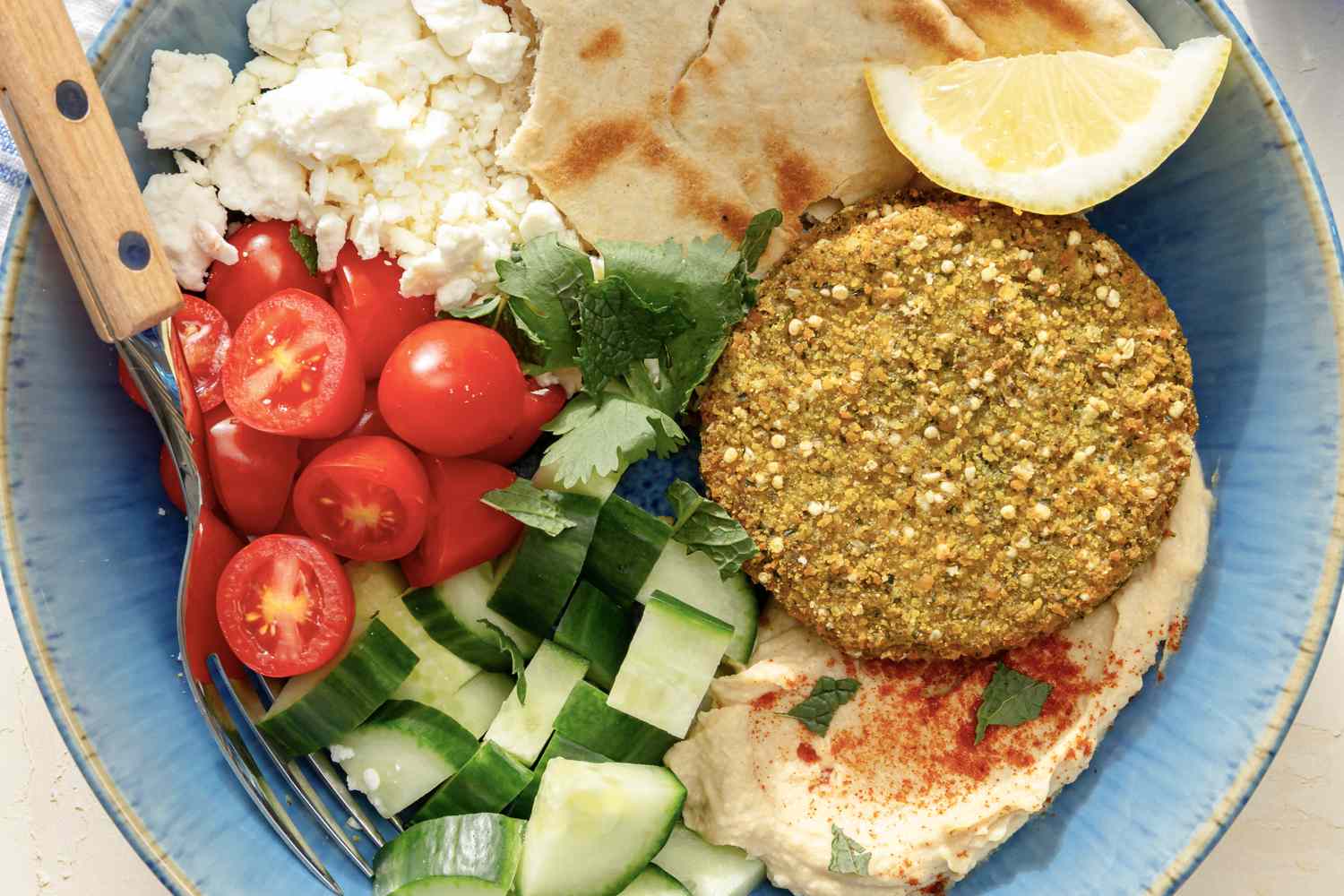 overhead view of Falafel Bowl - pita, feta, falafel, hummus, lemon slice, cucumbers, and grape tomatoes