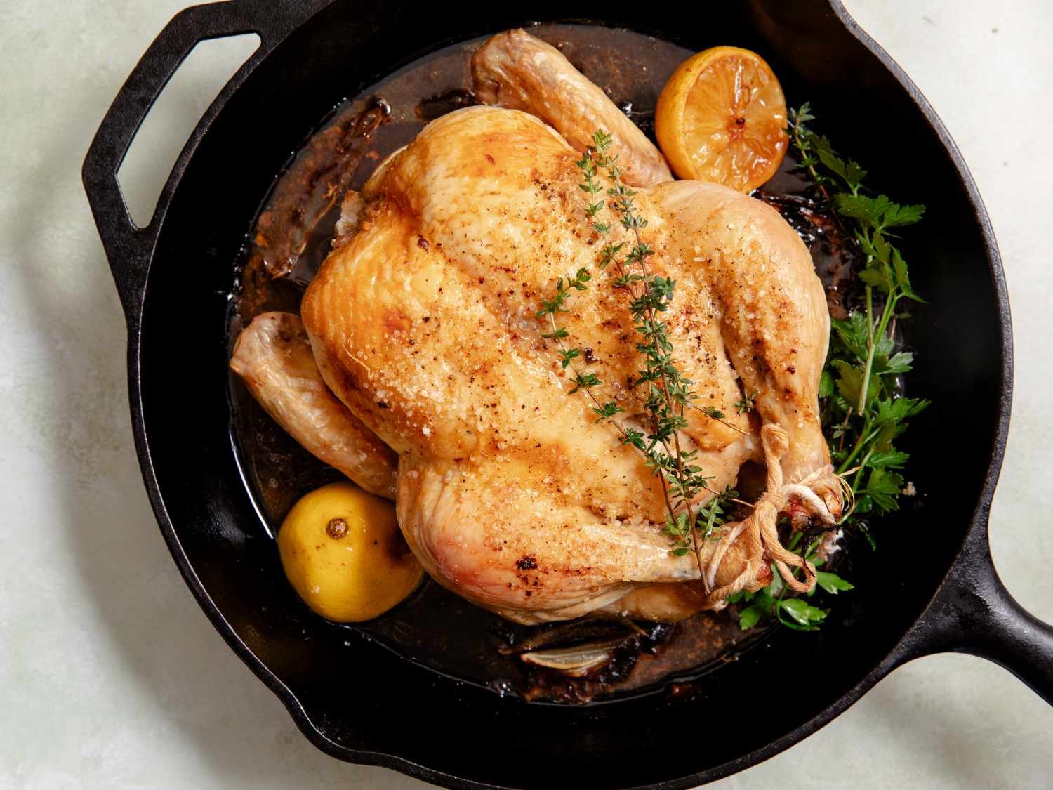 Overhead view of a whole roasted chicken with lemons and spices in a cast iron skillet