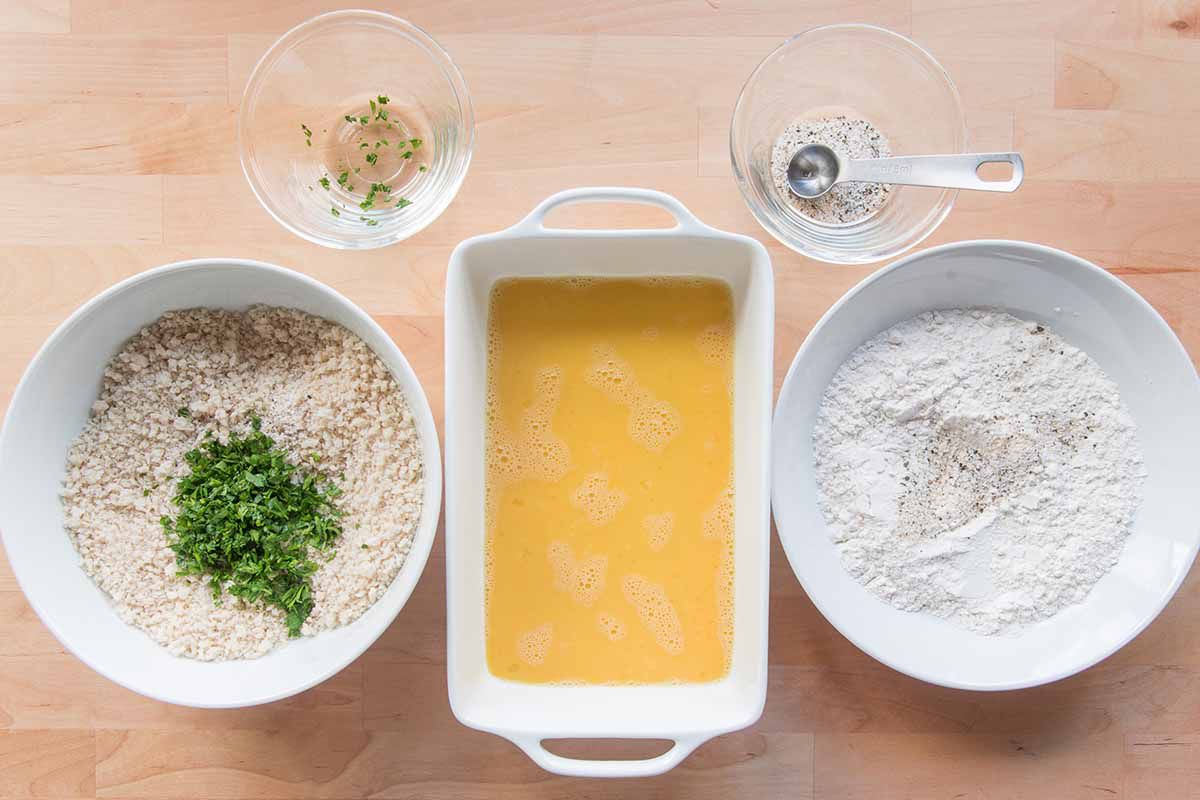 Three dishes lined up to batter chicken cordon bleu -- one with breadcrumbs, one with eggs and another with flour.