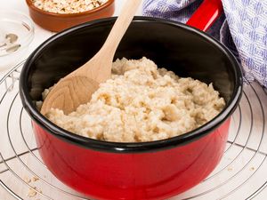 A red pot of oatmeal with a wooden spoon on a wire cooling rack