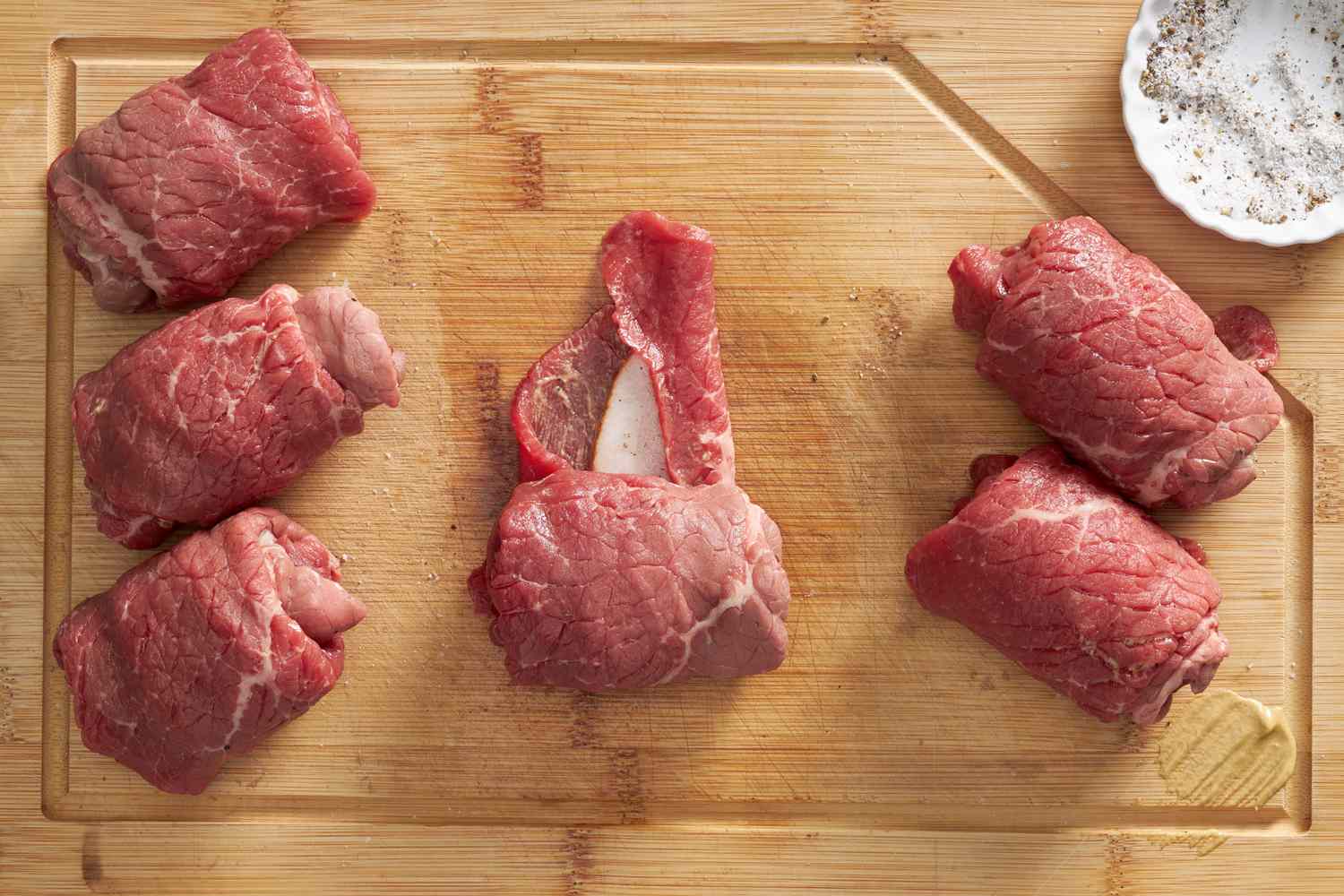 Making rouladen: starting from one end, beef is rolled over the filling (on a wooden cutting board next to already rolled rouladen) 