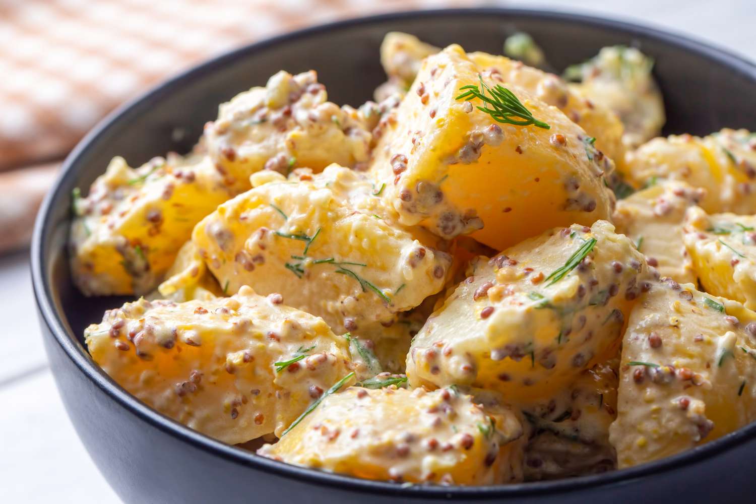 potato salad (mixed with mayo and mustard) in a bowl next to a checkered table napkin