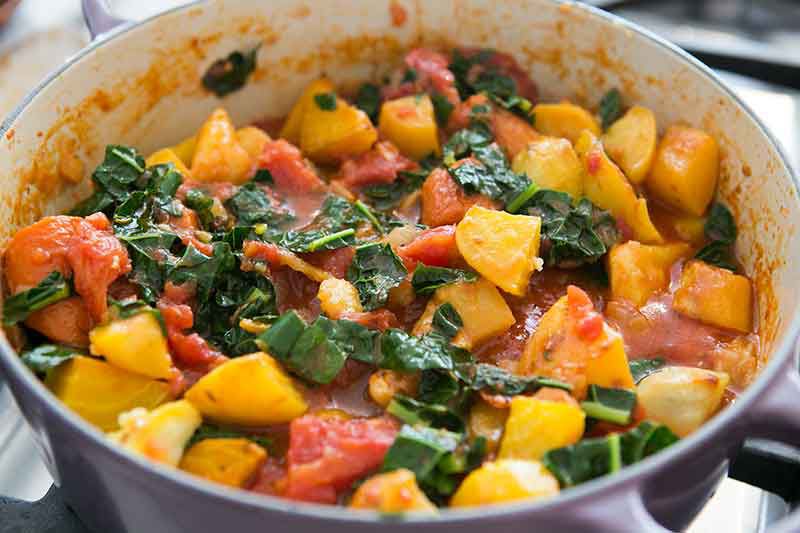 roasted root vegetables with tomatoes and kale in a pot