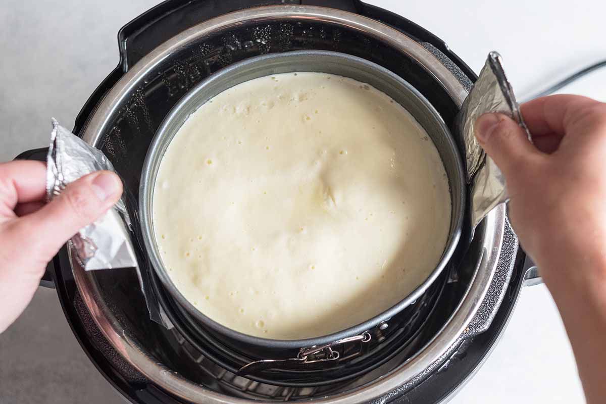 Cheesecake in the Instant Pot being removed by an aluminum foil sling