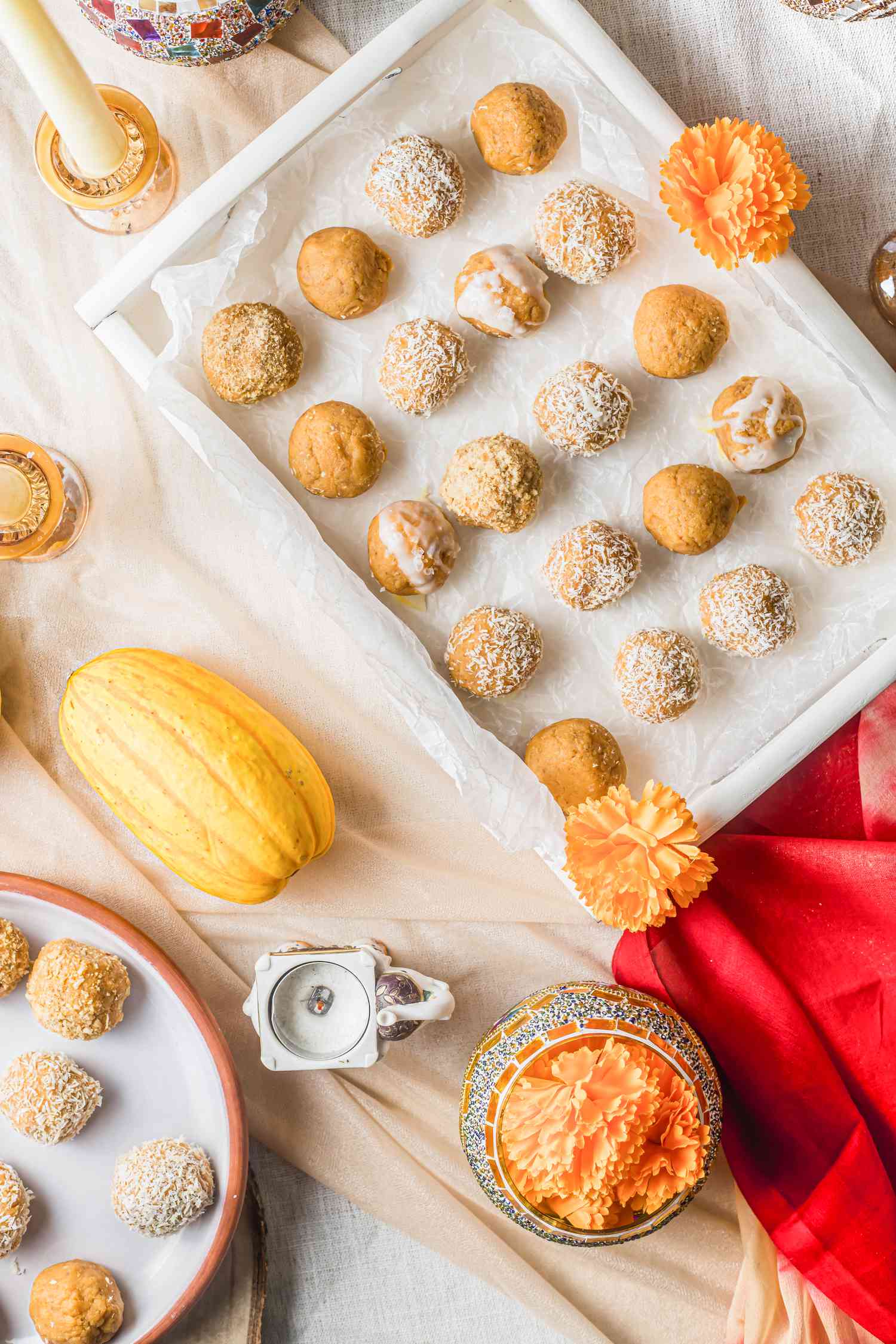Pumpkin Ladoo on a Tray and Plate Next to a Candle Holder, an Ornate Jar with Flowers, and a Delicata Squash 