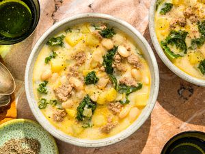 Overhead shot of two bowls with a cream based soup with beans, sausage, kale and potatoes