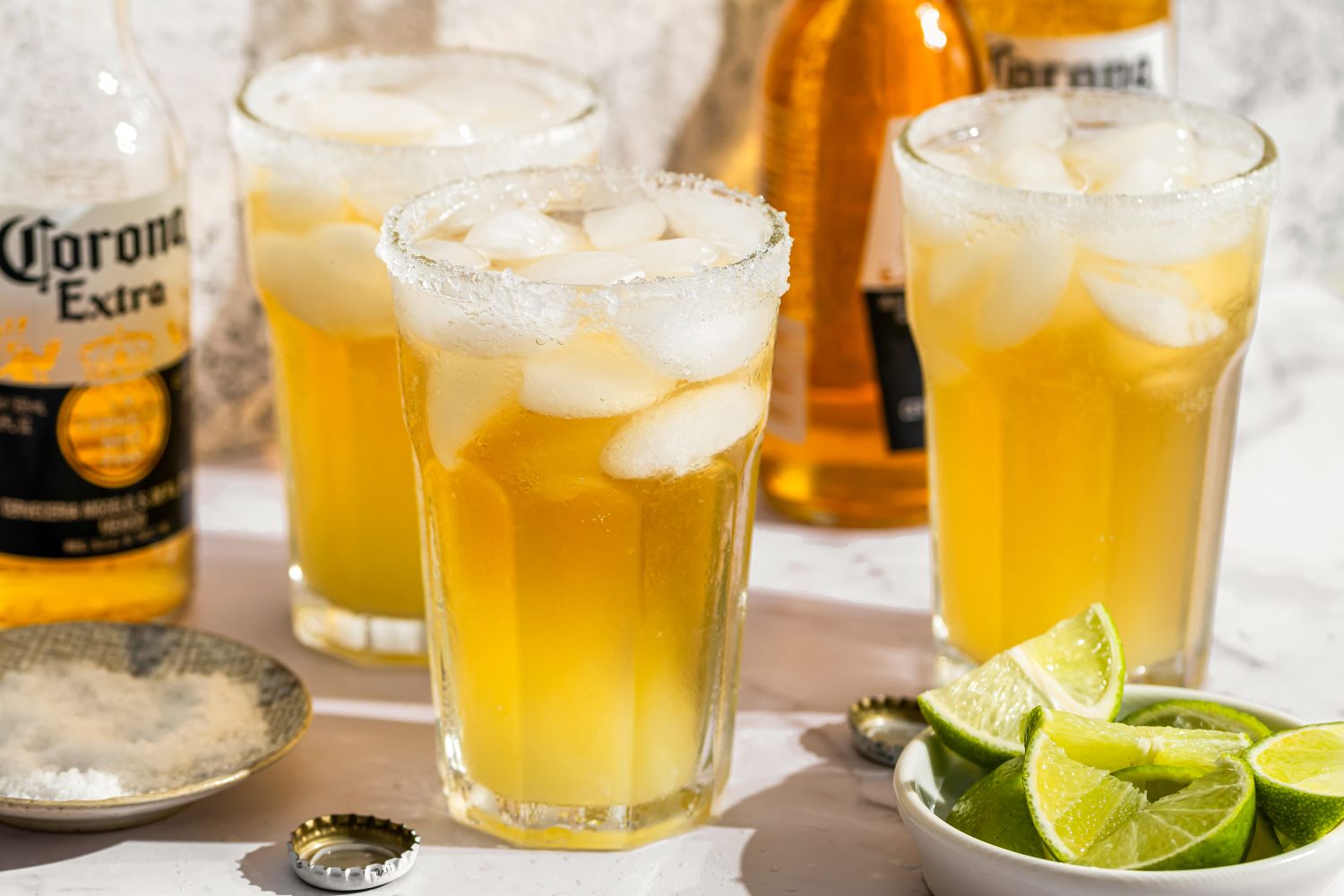Three glasses of Sueros, with bottles of Corona beer and lime wedges in the background