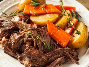 A plate of pot roast accompanied by roasted carrots and potatoes garnished with fresh herbs