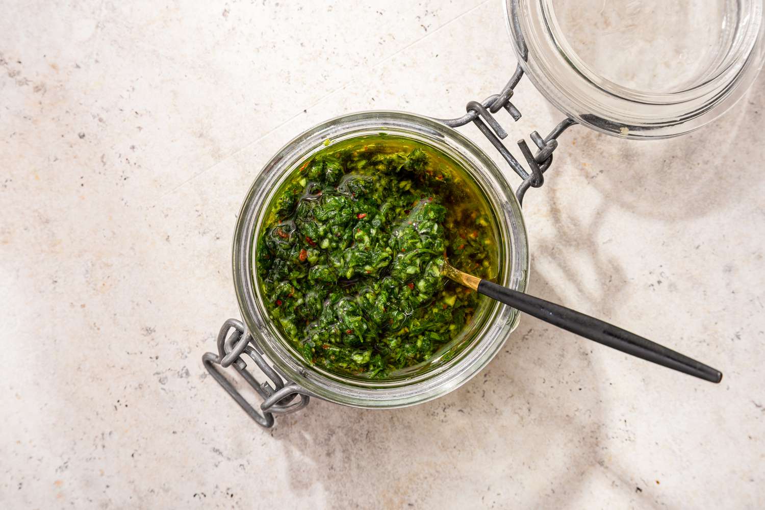 An open jar of chimichurri sauce with a spoon in it