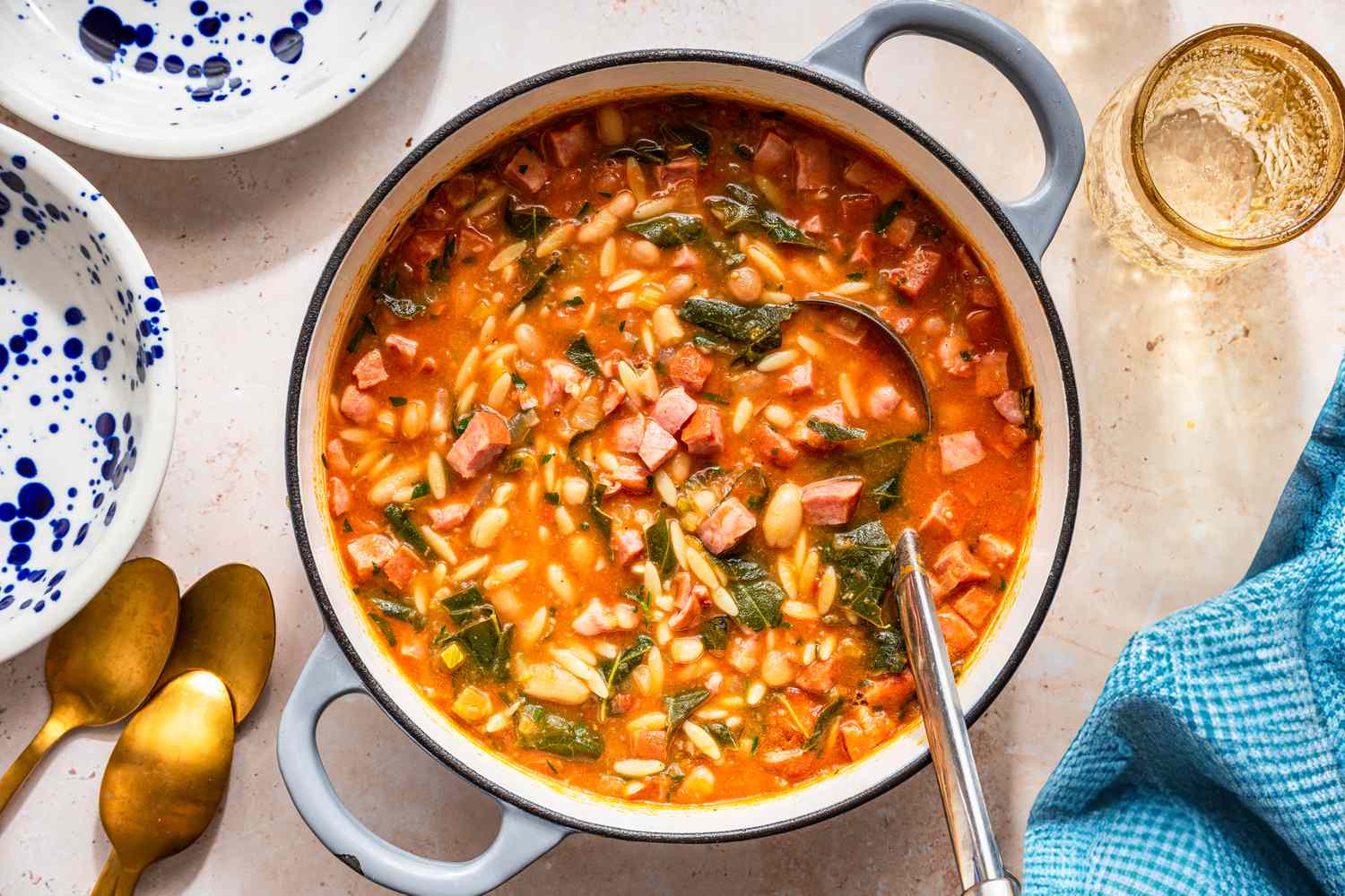 Swamp soup in a dutch oven at a table setting with bowls, a glass, utensils, and a kitchen towel