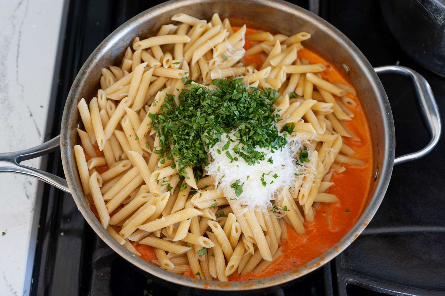 Penne, Basil, and Cheese Added to Vodka Sauce in Skillet