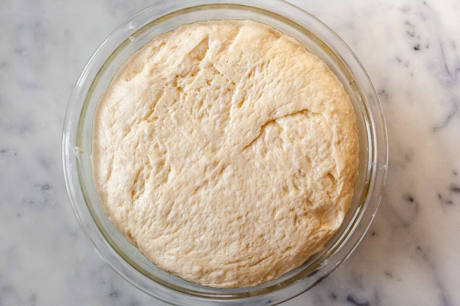 Risen dough for overnight milk bread cinnamon rolls with vanilla icing in a glass bowl.