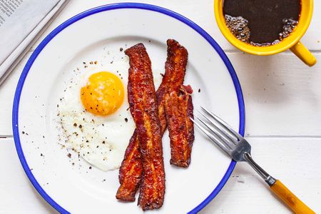 Over easy eggs on a blue rimmed plate with a side of bacon.