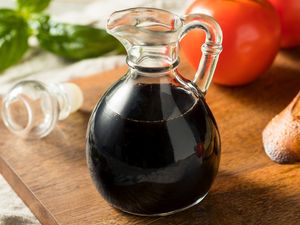 A glass carafe filled with balsamic vinegar placed on a wooden surface accompanied by tomatoes and basil leaves nearby
