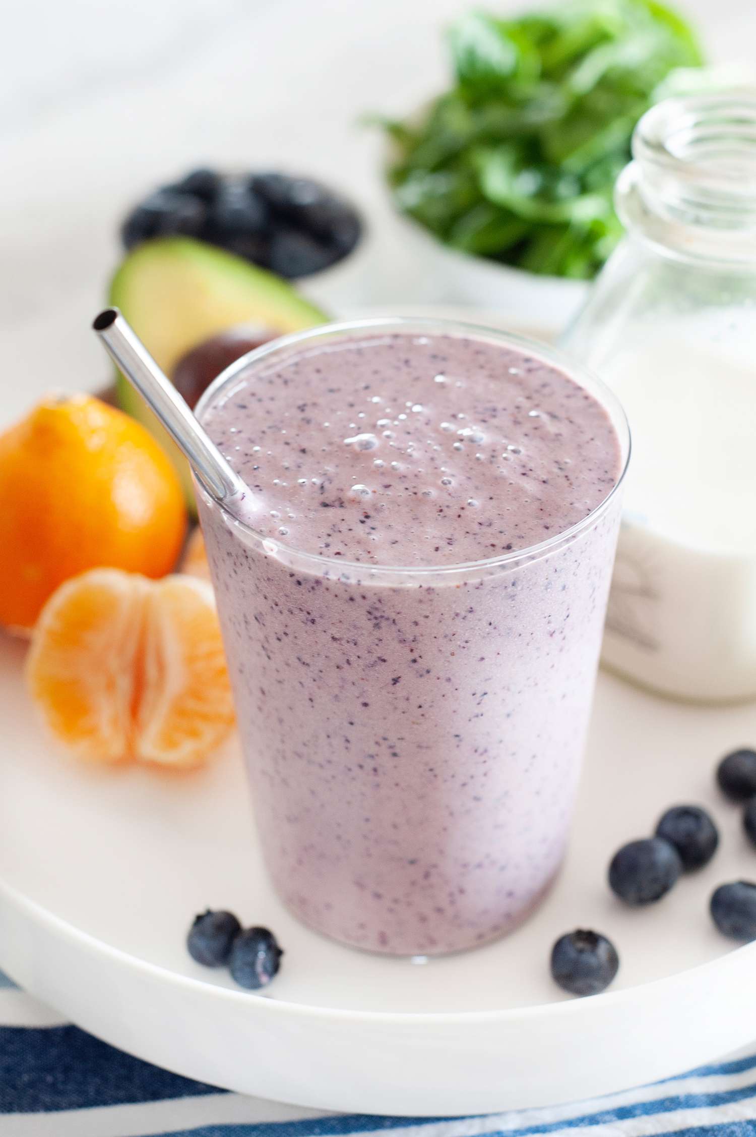 Blueberry breakfast smoothie on a tray along with fresh fruit and vegetables.
