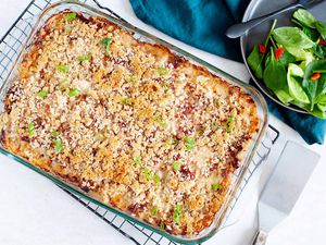 A golden brown baked reuben casserole is cooling on a rack. A metal spatula is in the lower right hand corner. A matte grey plate has a side salad and black fork in the upper right. A dark teal linen is under the plate.