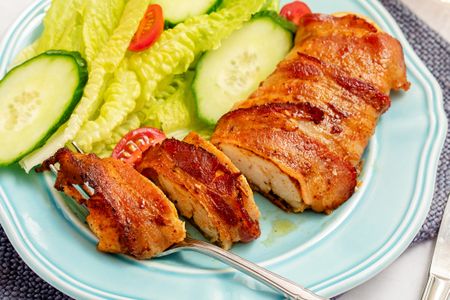 Baconwrapped chicken served with romaine lettuce cucumber and cherry tomato slices