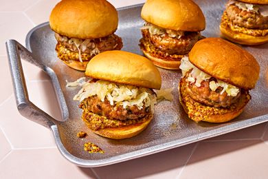 A serving tray with five sauerkraut topped bratwurst sliders