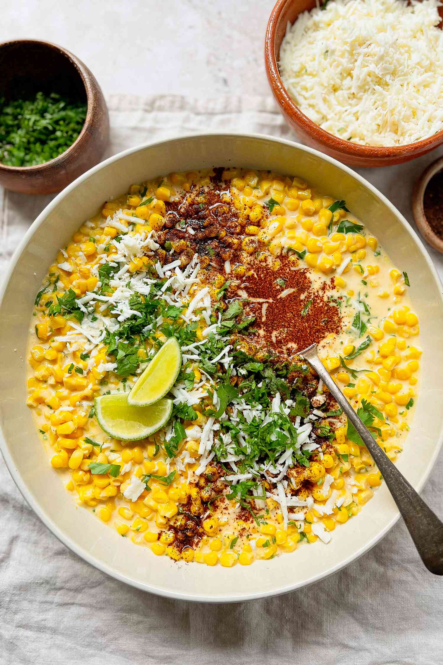 Bowl of Esquites Topped with Cilantro, Cotija Cheese, and Ancho Chile Pepper Surrounded by Bowls of Toppings