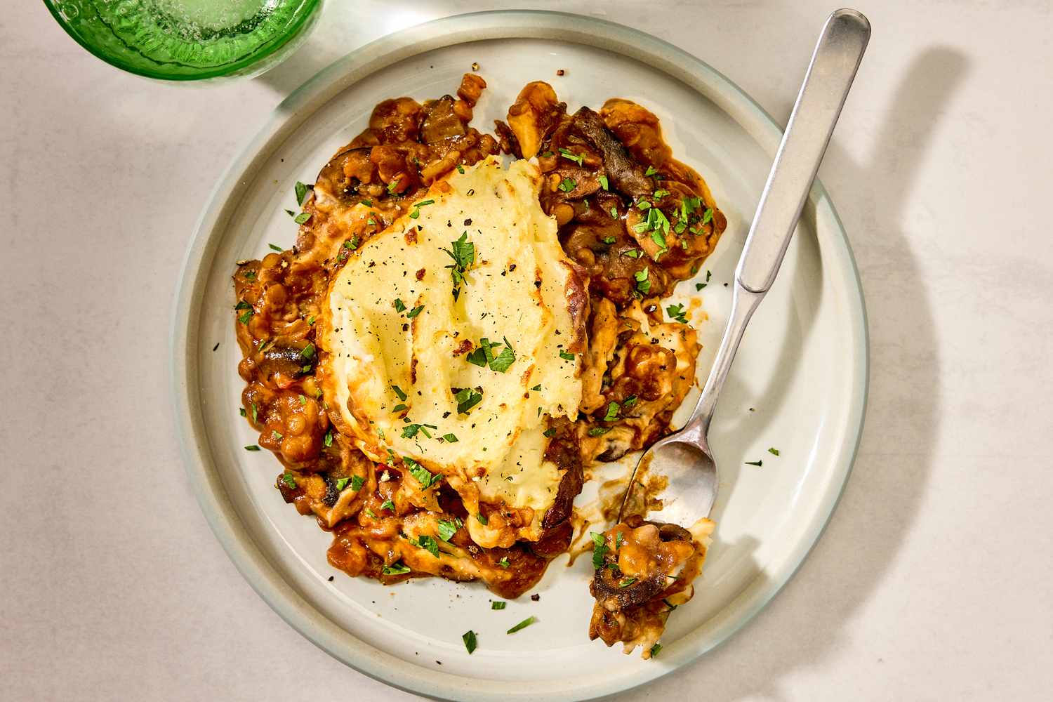 Overhead shot of a plate with a serving of lentil shepherd's pie, with a fork on the plate to the right