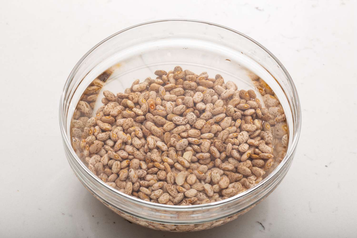 A white bowl of dried beans soaking in a glass bowl