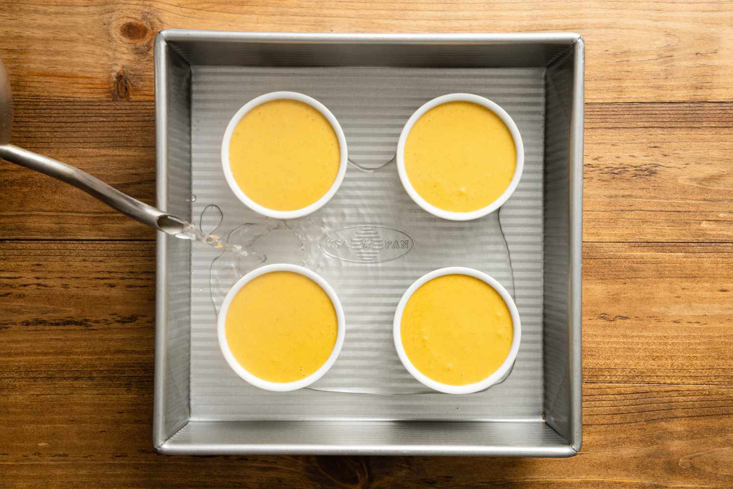 Four Ramekins Filled with Pumpkin Spice Creme Brulee Custard in a Baking Pan Being Filled with Water