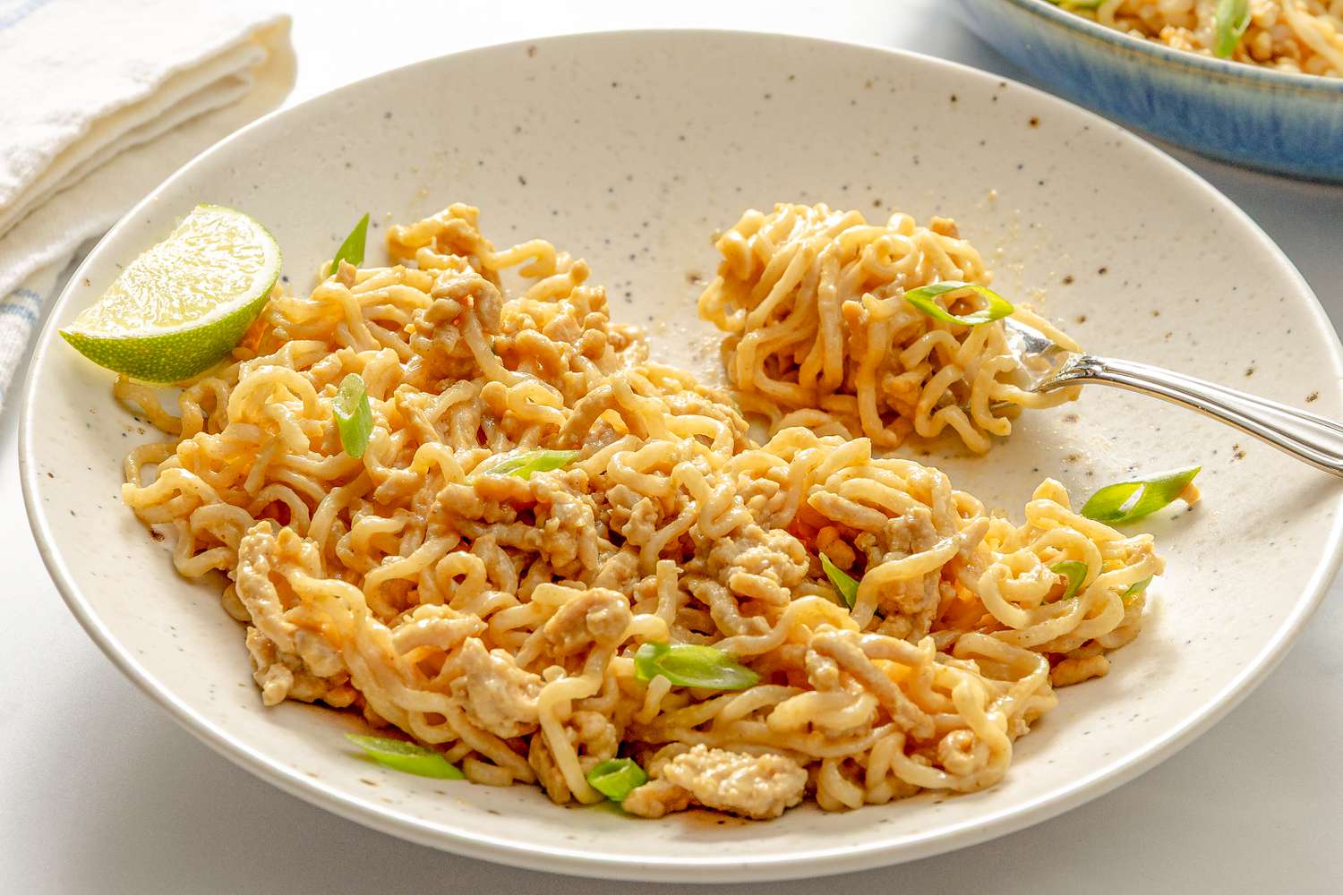 Noodles served with a peanut sauce, garnished with lime wedge and chopped scallions