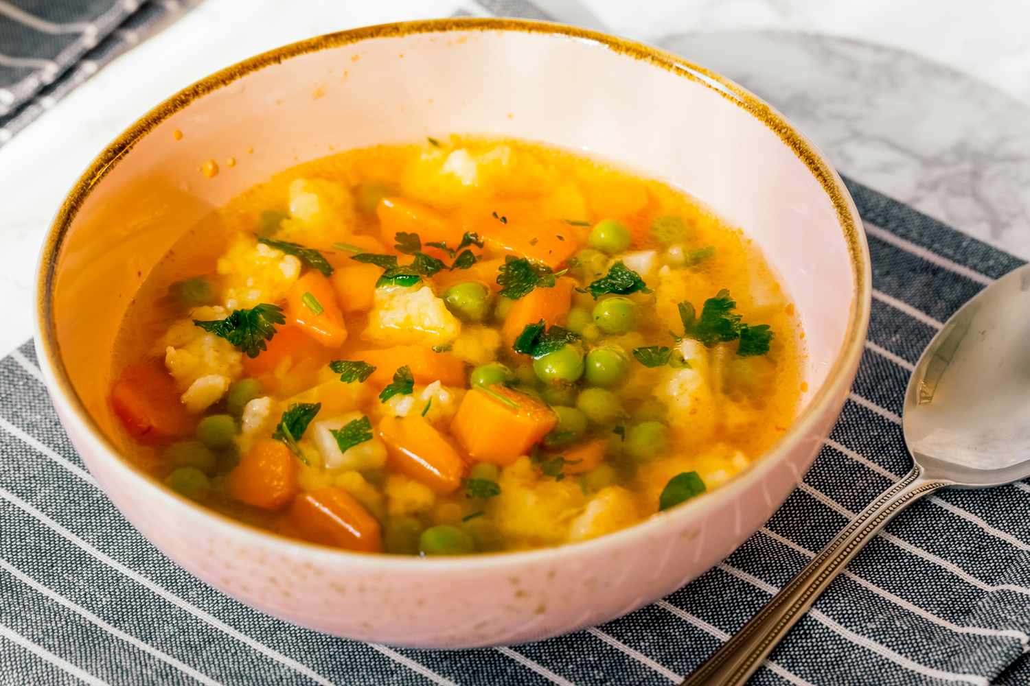 Bowl of vegetable soup with carrots peas and herbs on a striped cloth