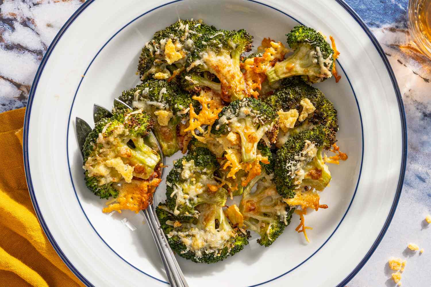 crispy parmesan broccoli on a plate next to a table napkin and a drink in a glass