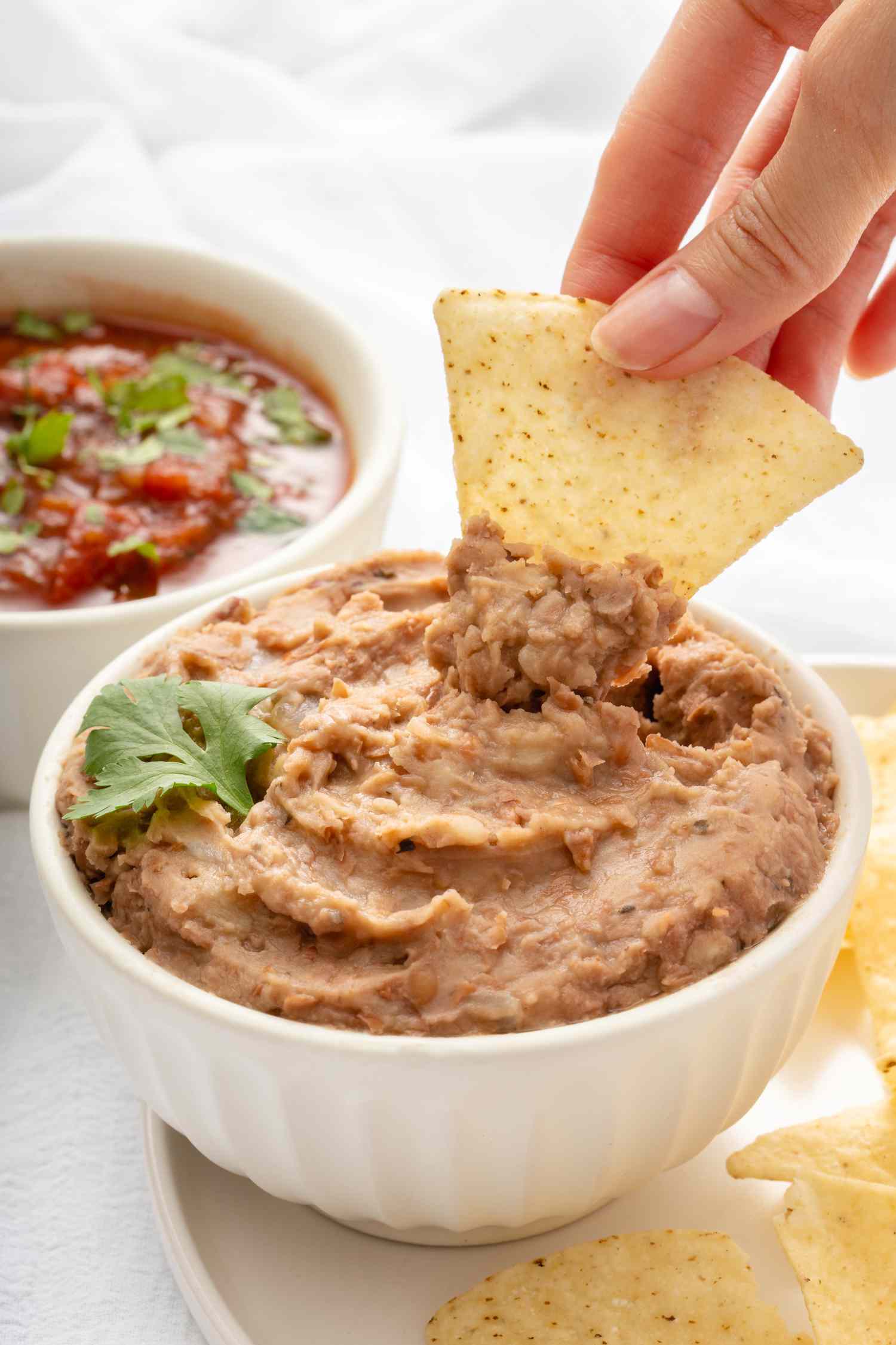 Dipping tortilla chip into a bowl of homemade refried beans.