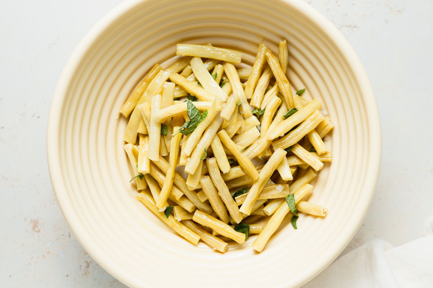 Overhead view of yellow beans in a cream colored bowl.