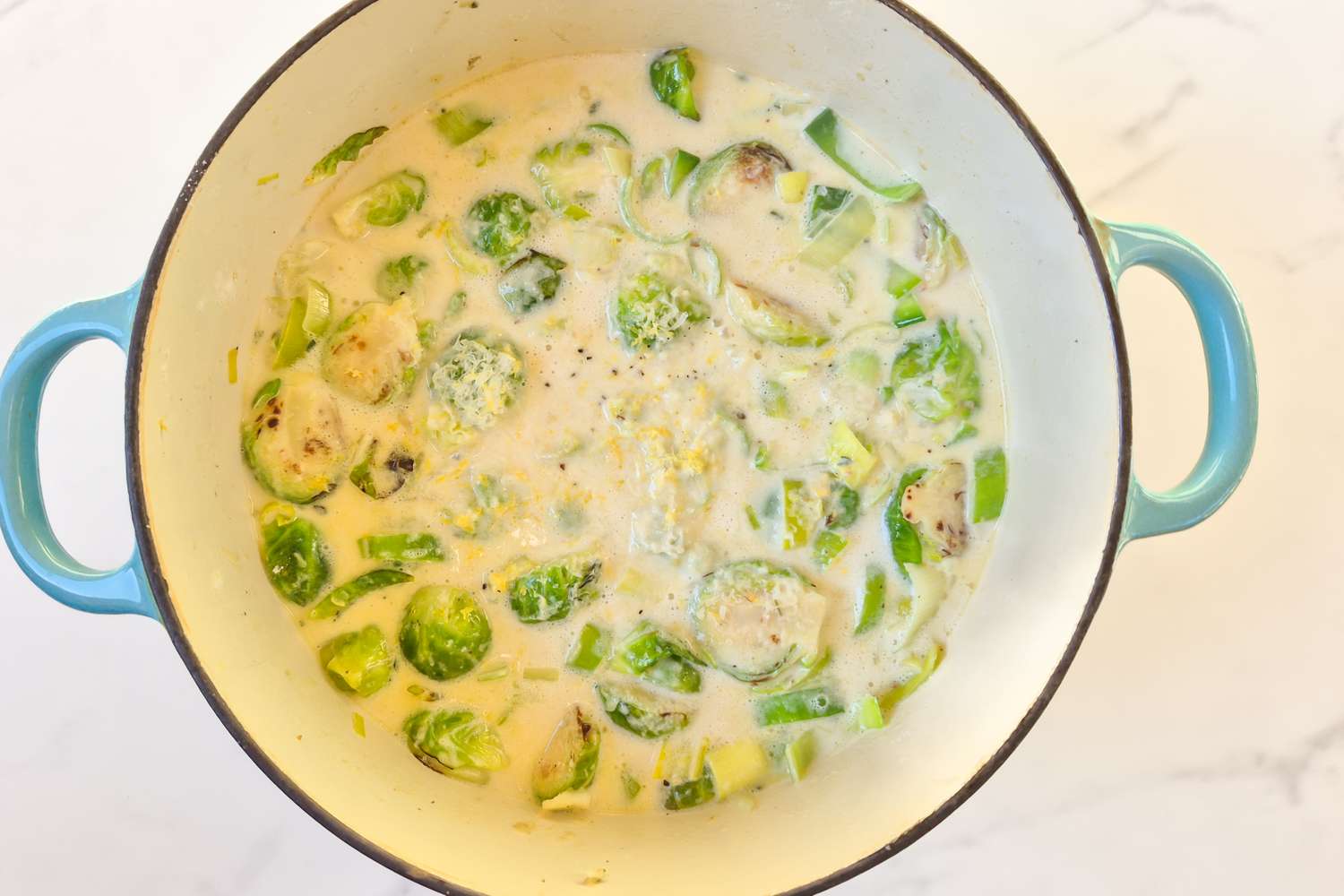 Brussels sprouts in creamy sauce cooking in a pot with blue handles