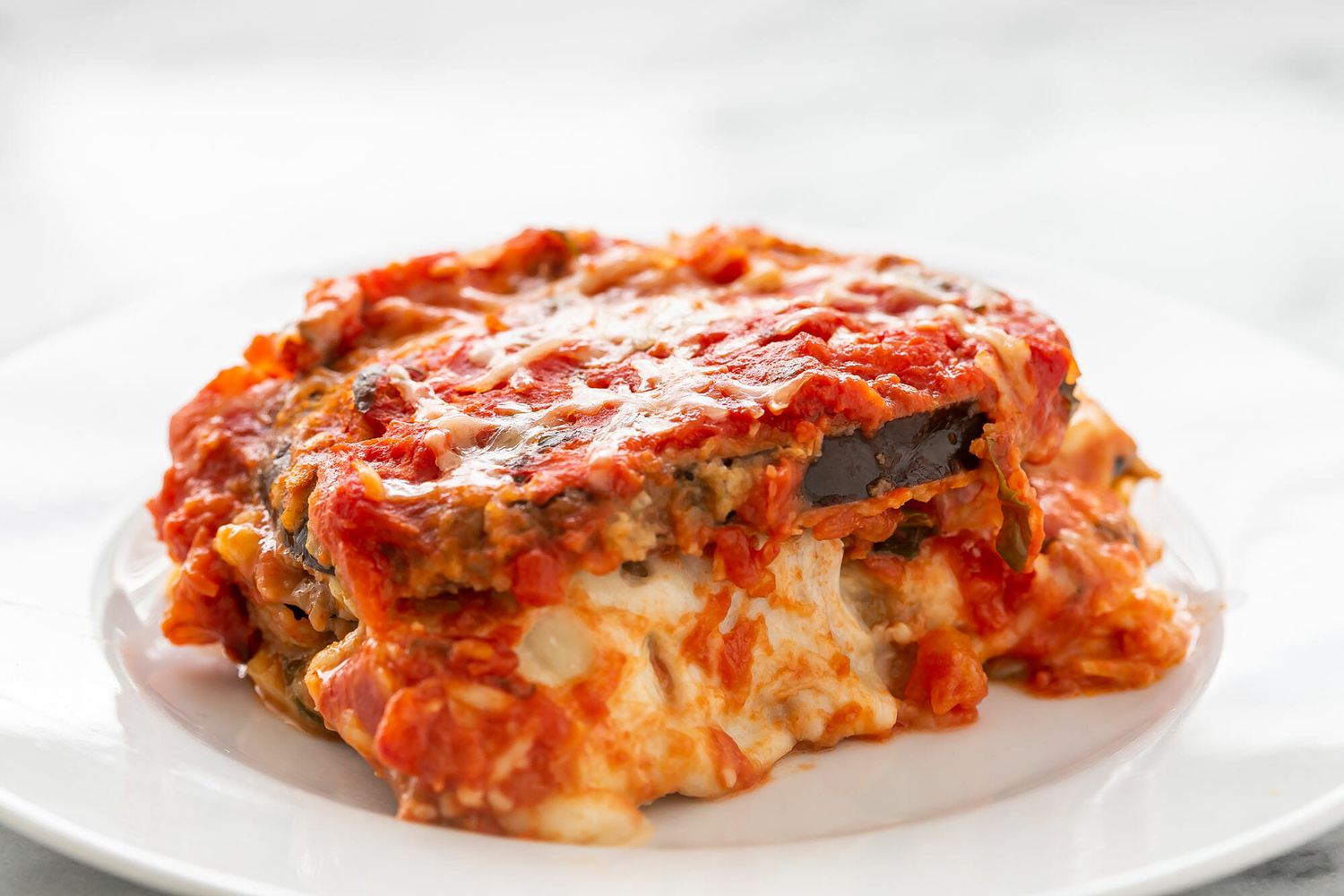 A slice of eggplant parmesan on a white plate